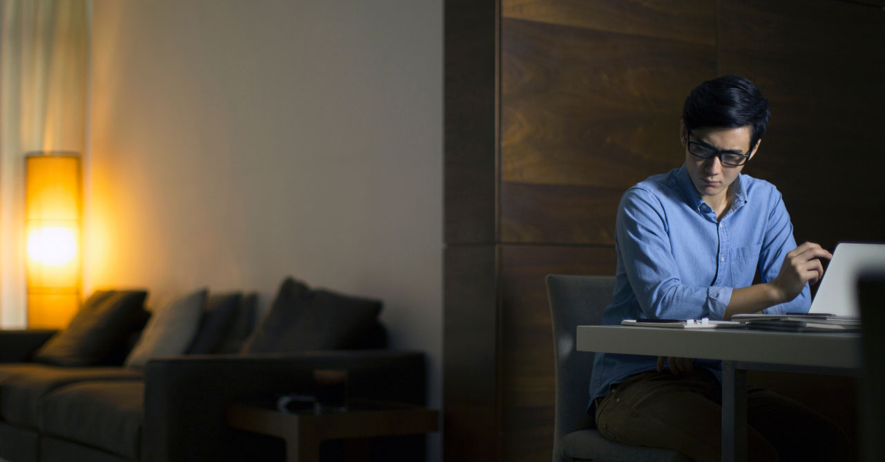 Asian man sits at laptop in darkened room