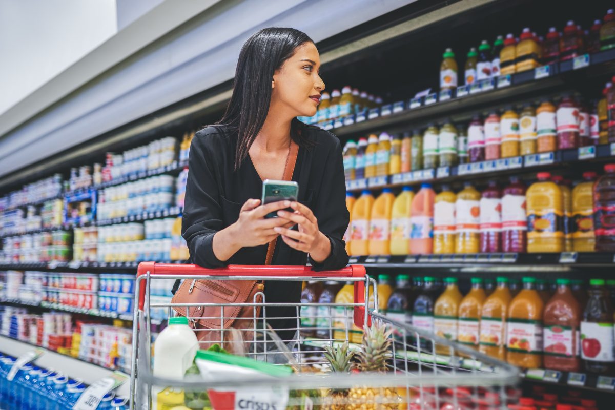 A young woman USES a smartphone while shopping in a grocery store