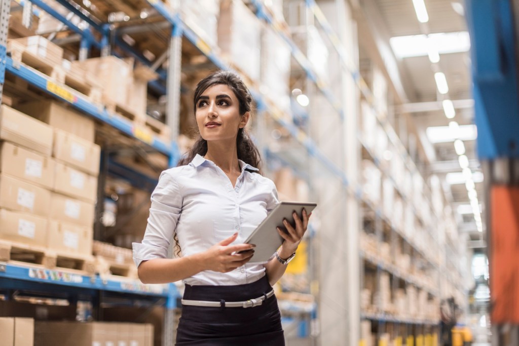 Woman with tablet in factory storehouse looking around