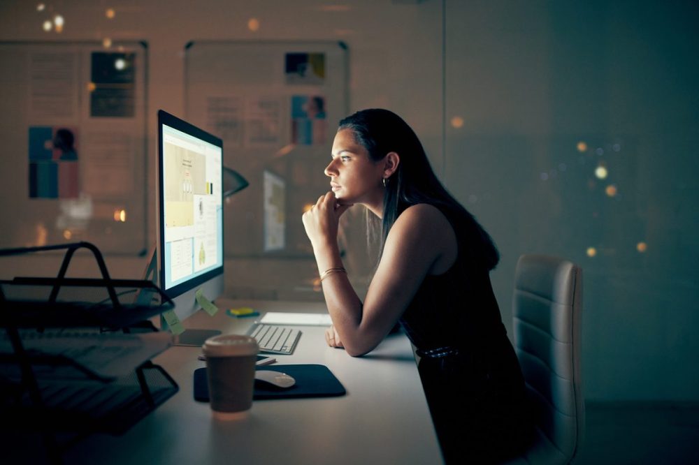 Shot of a young businesswoman using a computer at night in a modern office