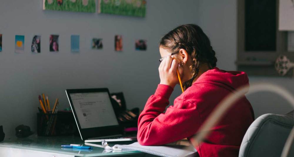 Girl with red hoodie holding pencil with braids looking at laptop