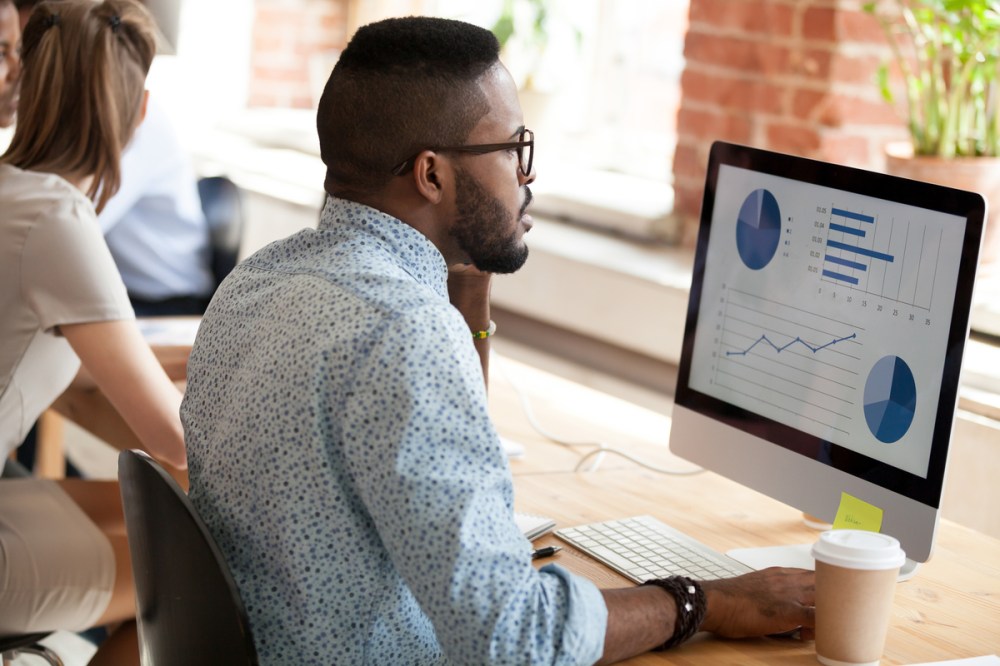 A black man in glasses looking at charts on his computer preparing for a category review.