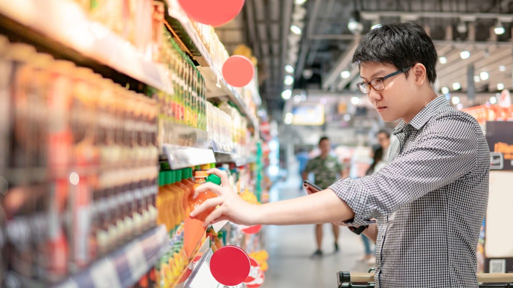 An Asian man reaches for a breakthrough innovation product on a grocery store shelf.