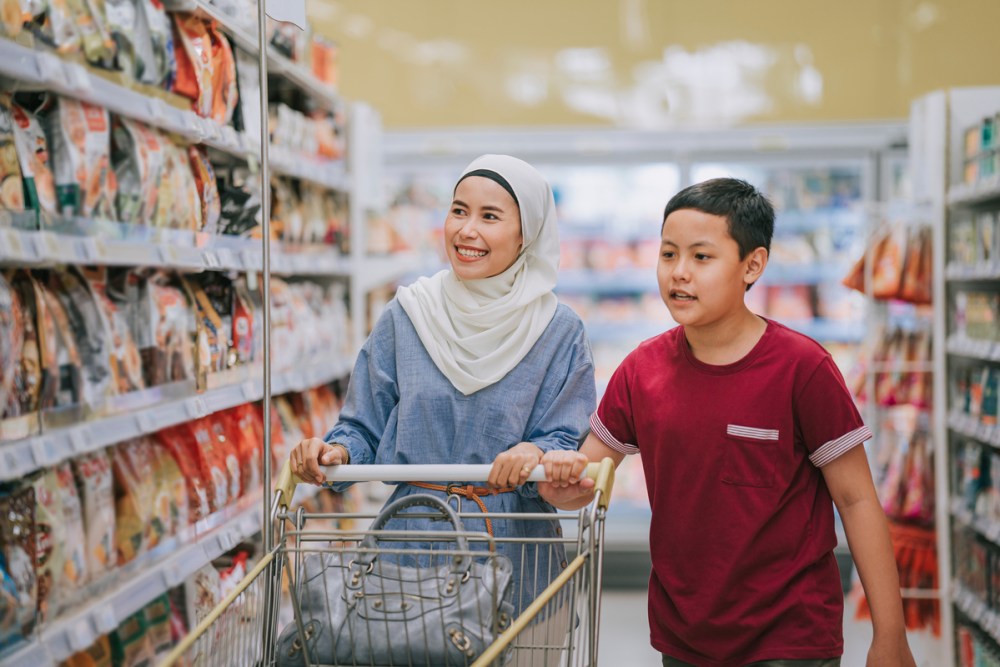 malay mother with hijab and son pushing shopping cart shopping in supermarket during weekend