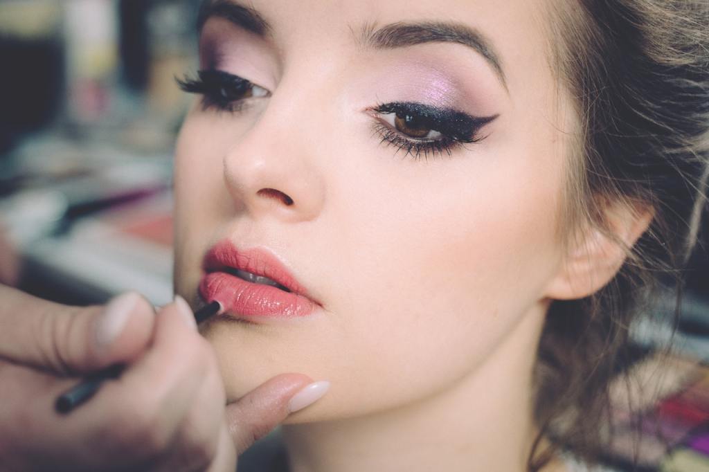 A woman wearing eyeshadow applies lipstick