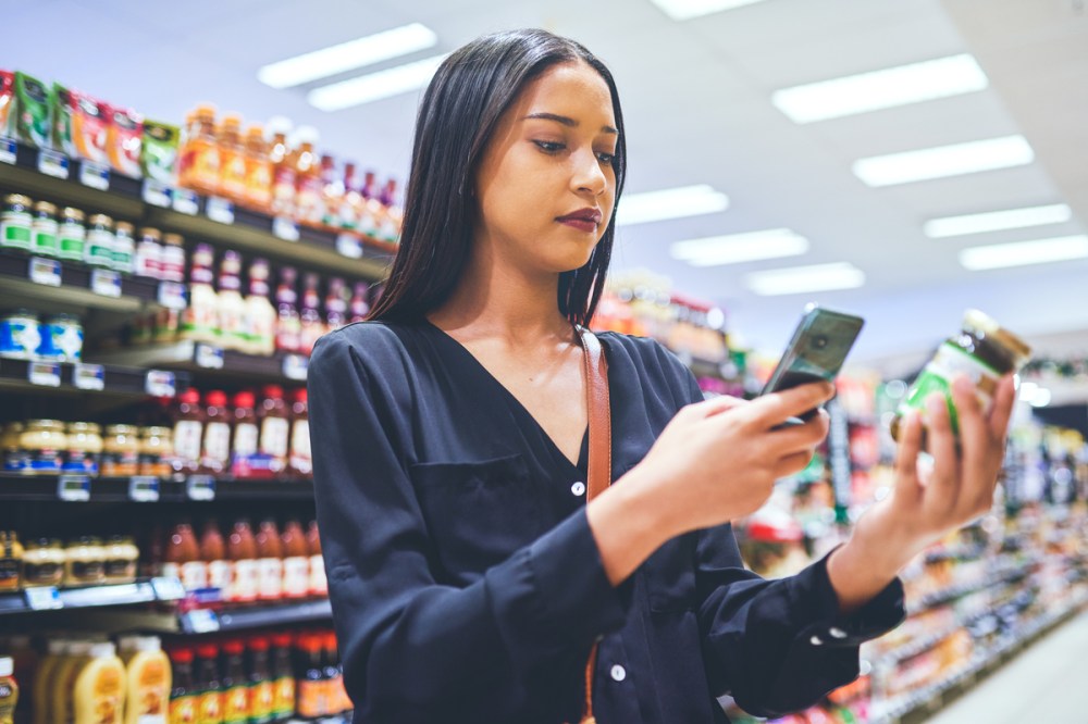 A young woman using a smartphone while shopping in a grocery store