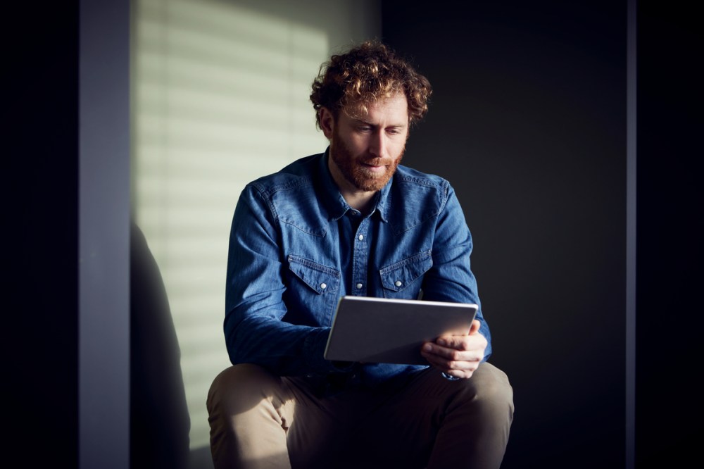 Casual businessman sitting down using a tablet to shop e-commerce
