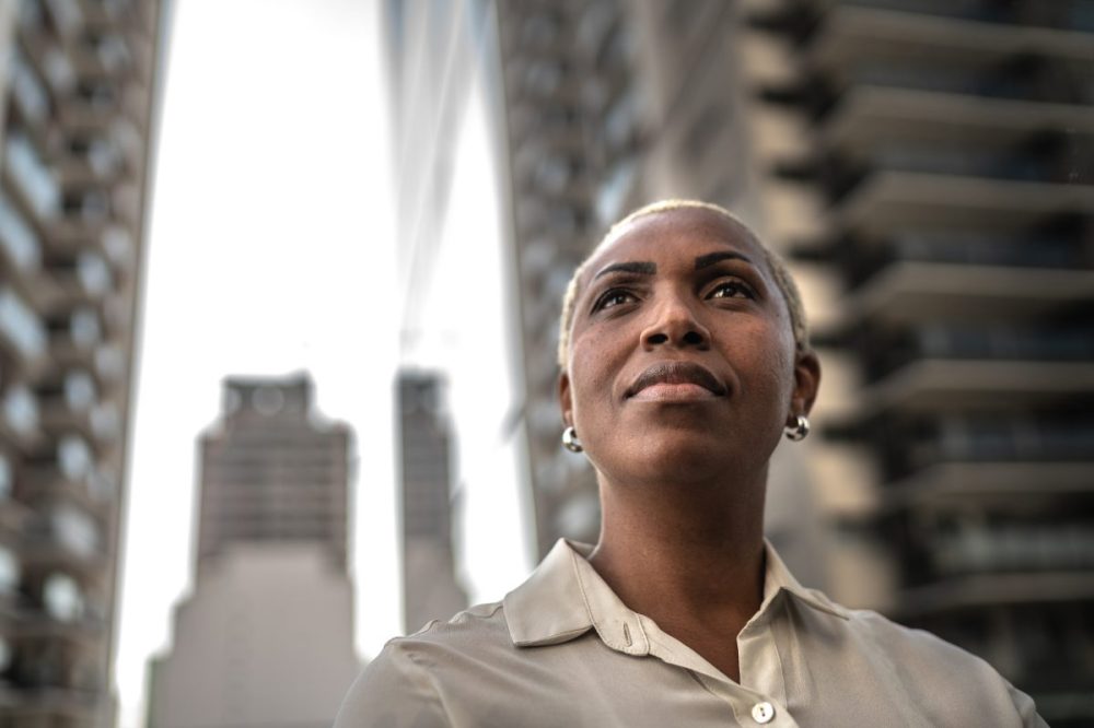 A woman looking forward intently while standing among tall buildings in a city