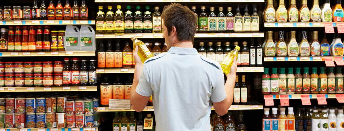 Man with blue shirt holding product looking at the label in a store aisle