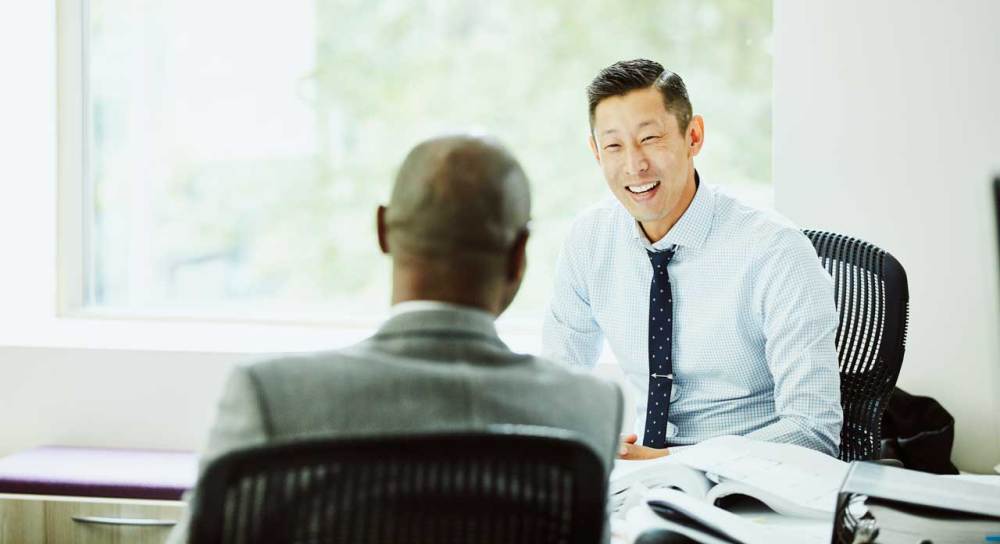 Asian business man with tie meeting with a bald dark-skinned man in a conference room.
