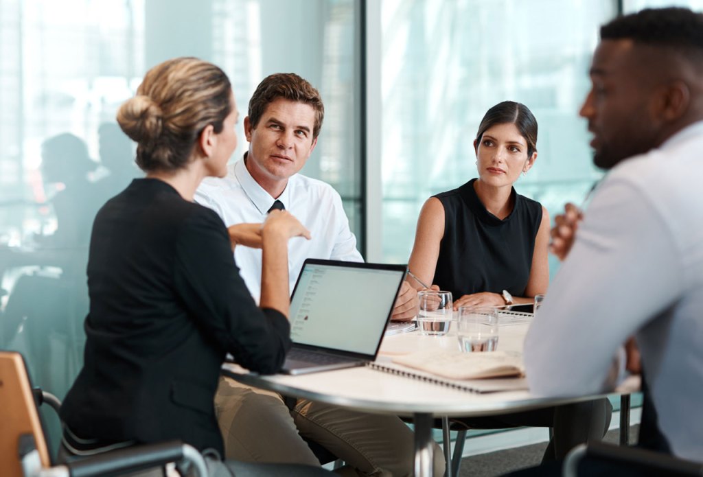 Conference room meeting with woman at laptop leading a conversation with 3 others