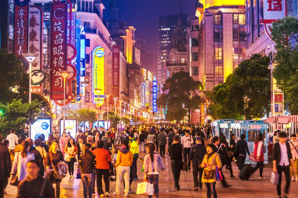 Crowds walk below neon signs on Nanjing Road. The street is the main shopping district of the city and one of the world's busiest shopping districts.