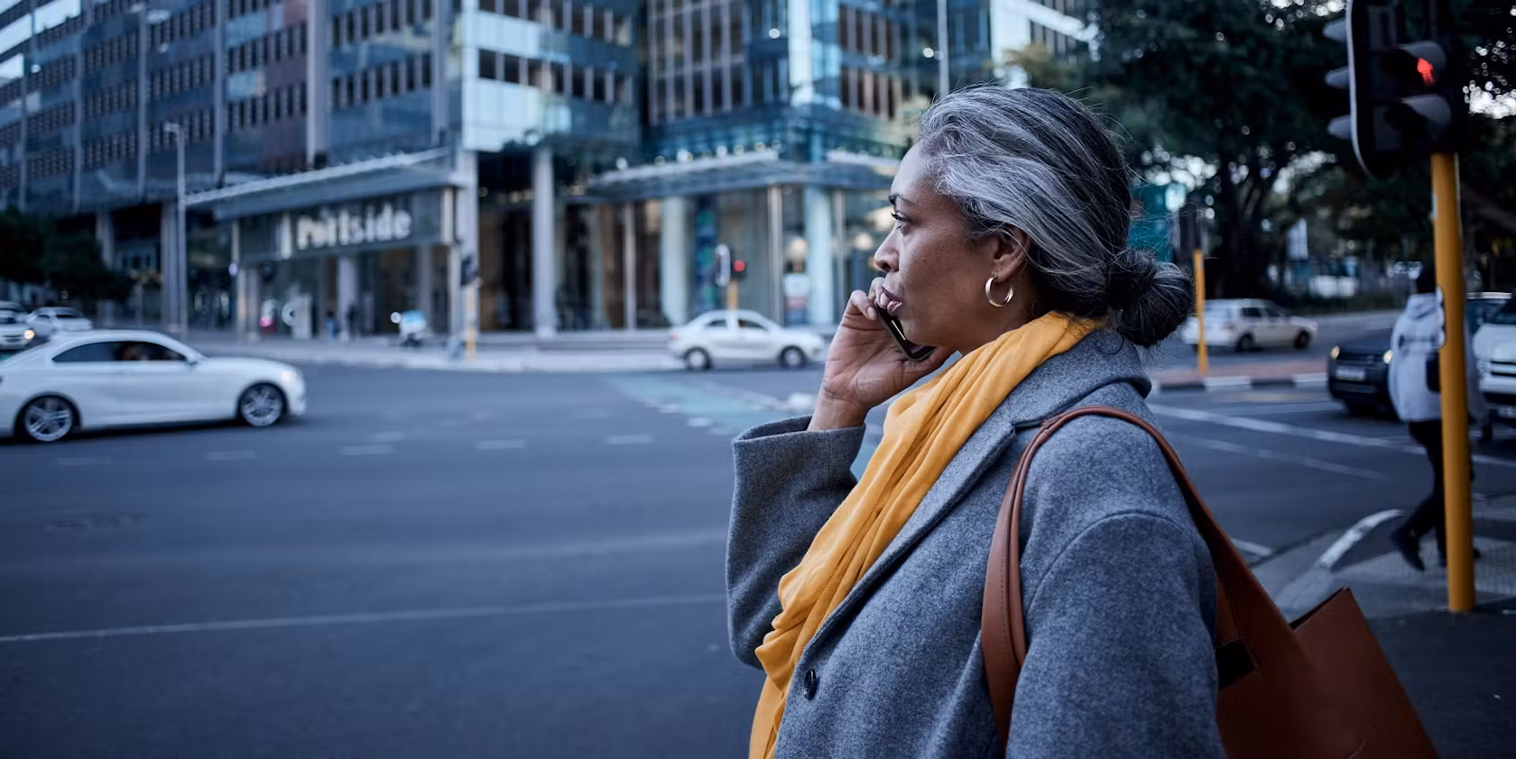 Woman with think wool coat and yellow scarf on mobile walking on the street with a leather handbag on her shoulder