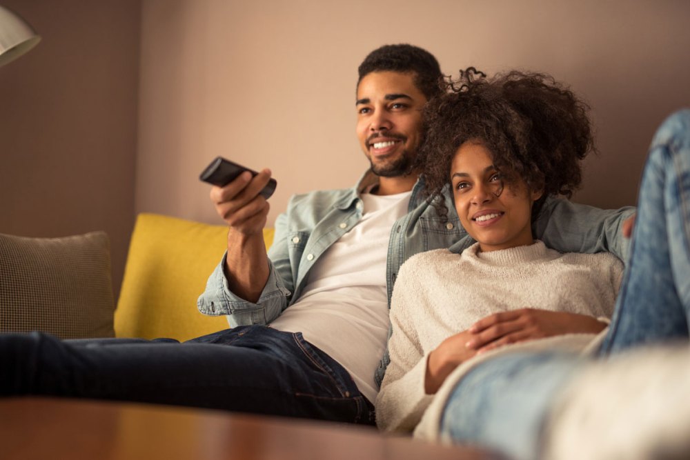 A couple relaxes together on a sofa watching teleevision