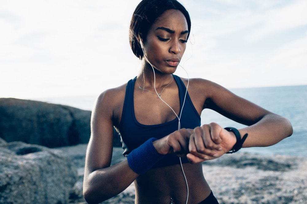Fit African-American woman checks her watch on a run with white earpods