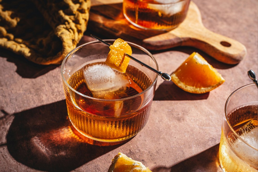 Cognac on the rocks with a twist of orange peel sat on a wooden counter