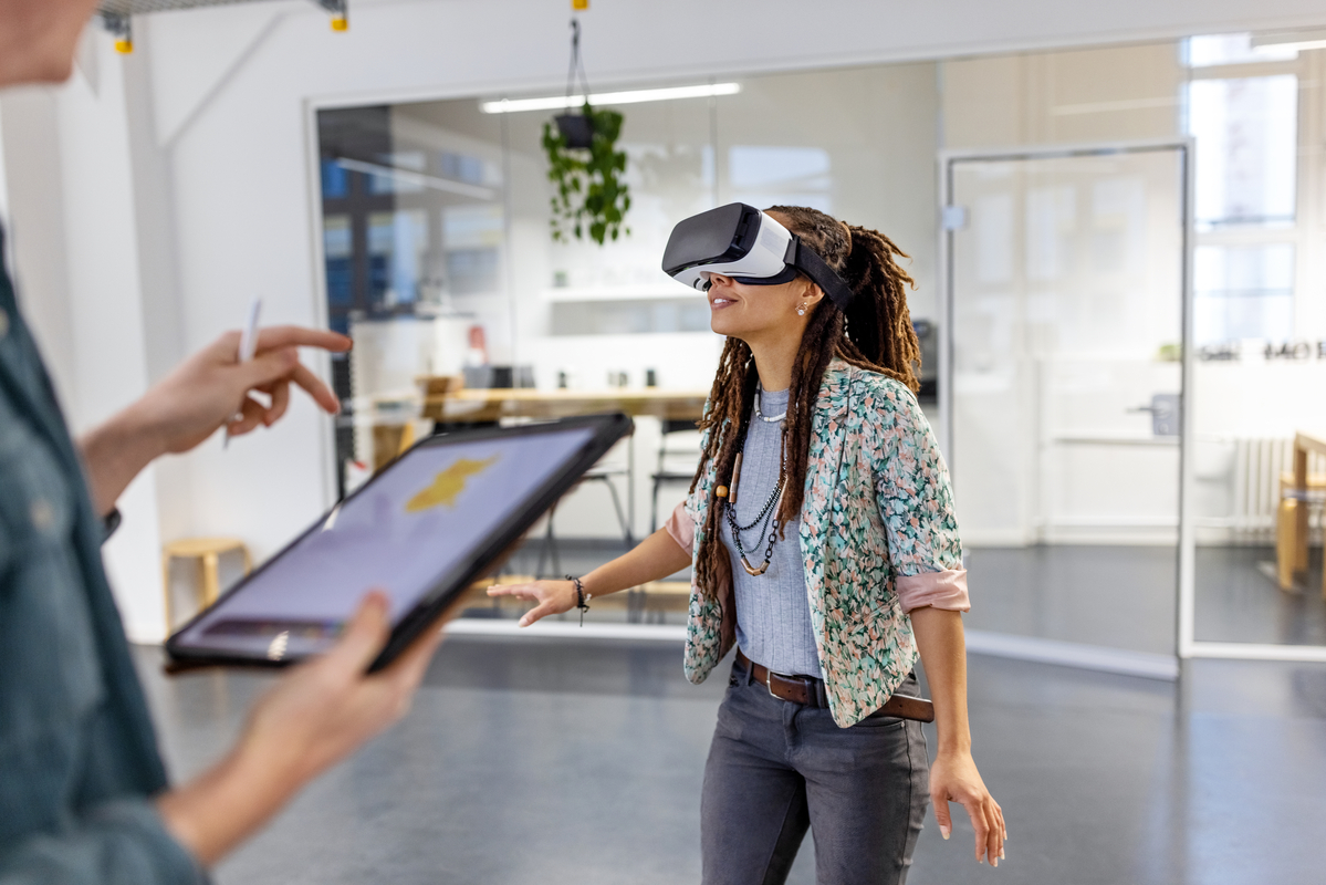 Young woman wearing virtual reality headset by a male colleague using digital tablet. Startup business colleagues testing out virtual reality glasses in the office.